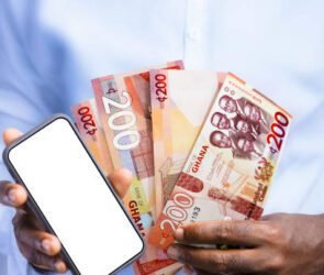 A man holding a smartphone with the Ghanaian Cedis Cash