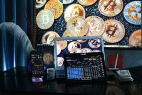 A computer device showing crypto trading with different cryptocurrencies in the background of the picture.