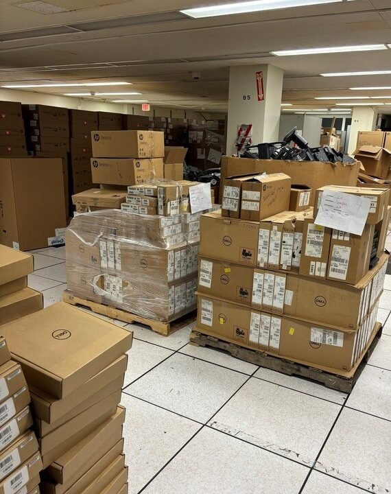 Pallets of laptops and other IT devices in an ITS storage facility, many never opened or lightly used, scheduled for destruction.