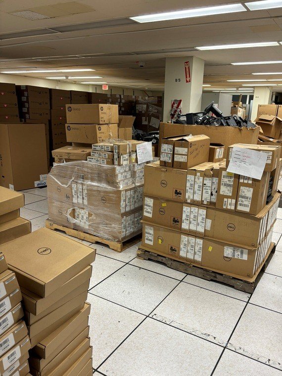 Pallets of laptops and other IT devices in an ITS storage facility, many never opened or lightly used, scheduled for destruction.